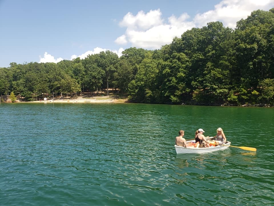 Group rowing a small boat on forested lake near shoreline