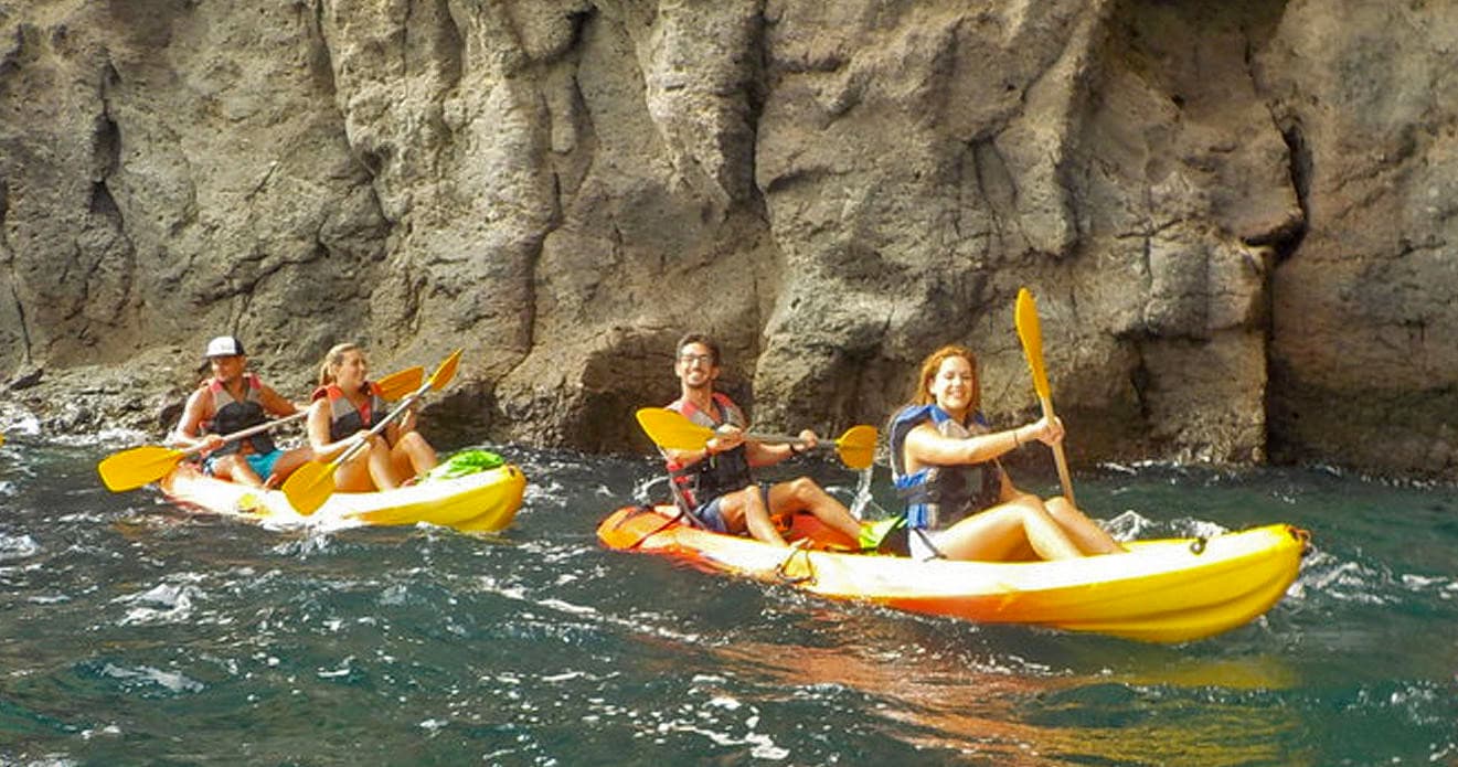 Sea kayakers paddling through coastal cave and rocky cliffs