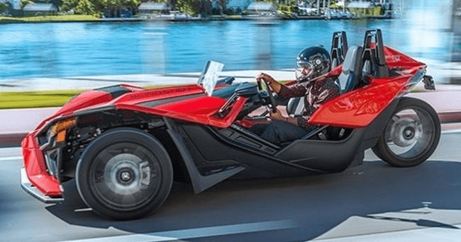 Red Slingshot roadster driving along coastal highway in sunlight