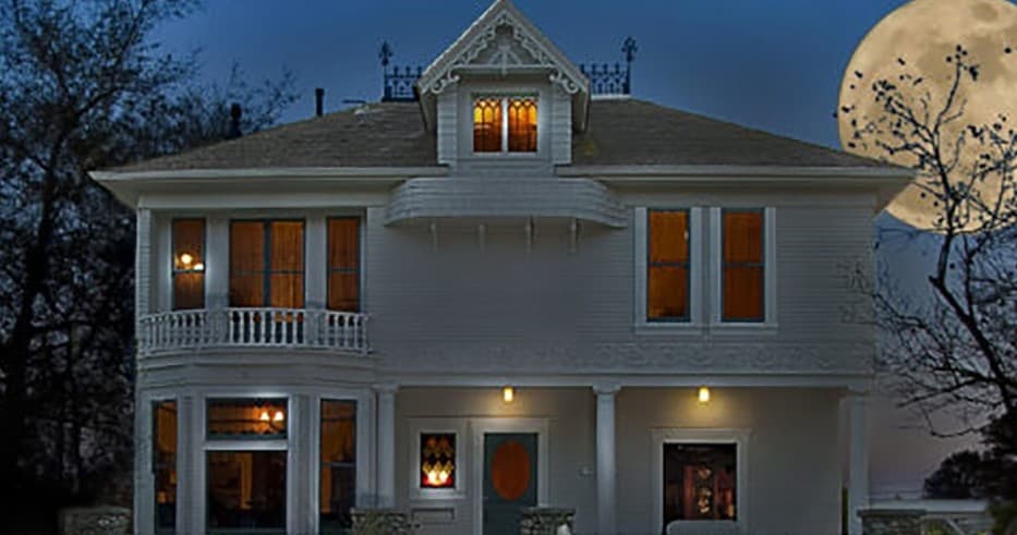 Creepy Victorian house exterior lit at night with full moon backdrop