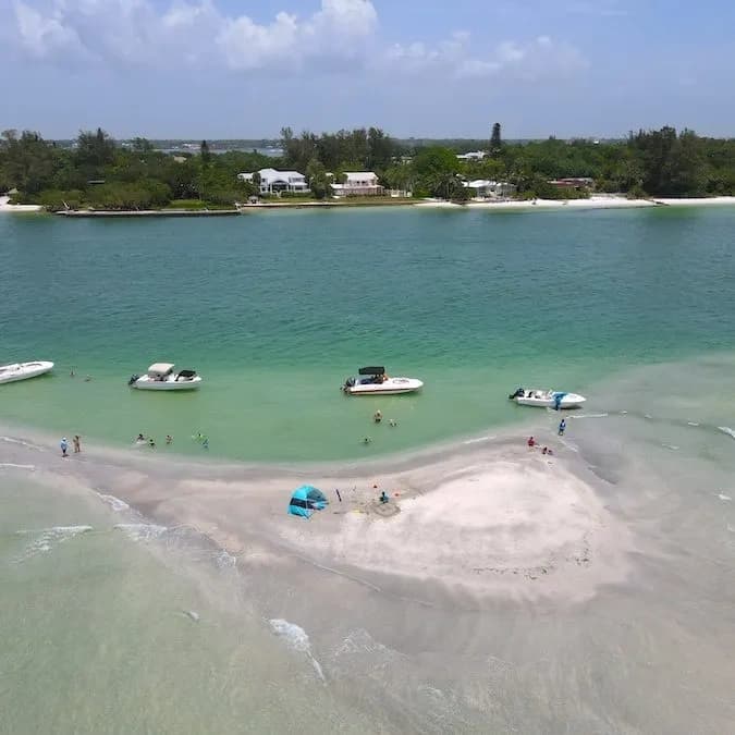 Sandbar with anchored boats and beachgoers in coastal inlet