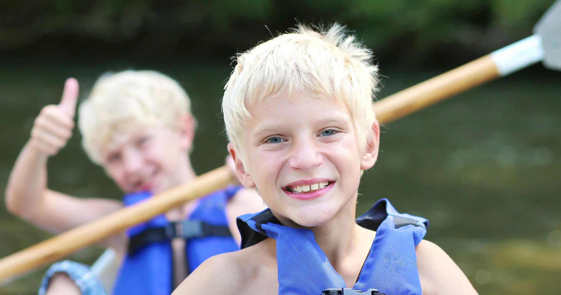 Children in life jackets smiling and paddling a kayak on calm water
