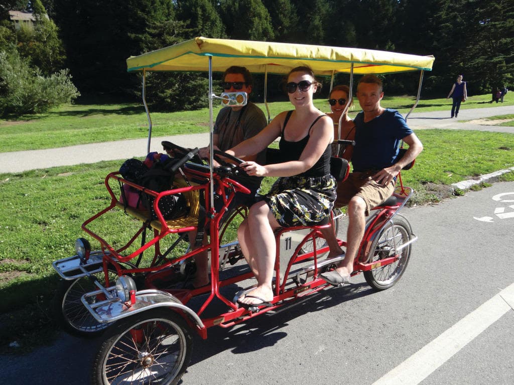 Four-person surrey bike tour on sunny park path with riders