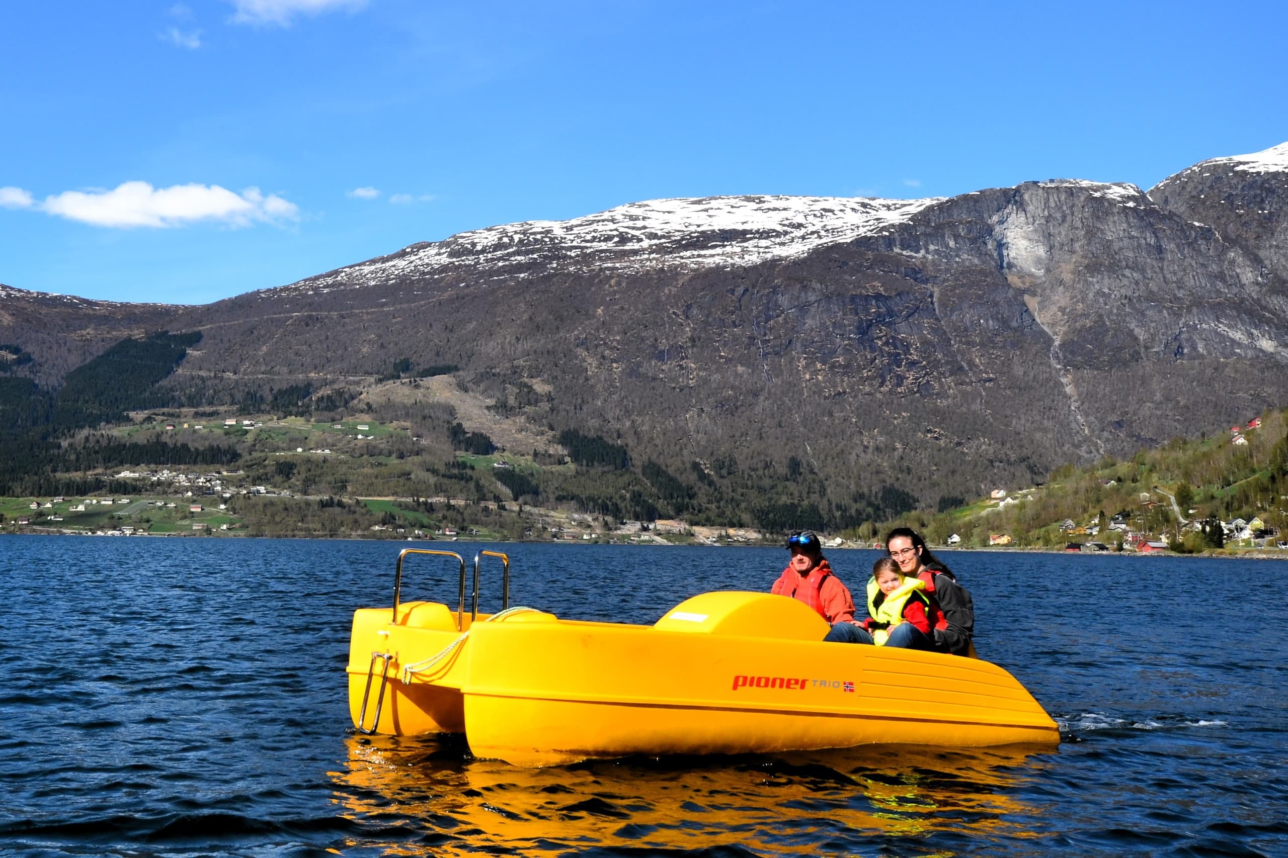 Bright yellow pedal boat on calm fjord with snow-capped hills