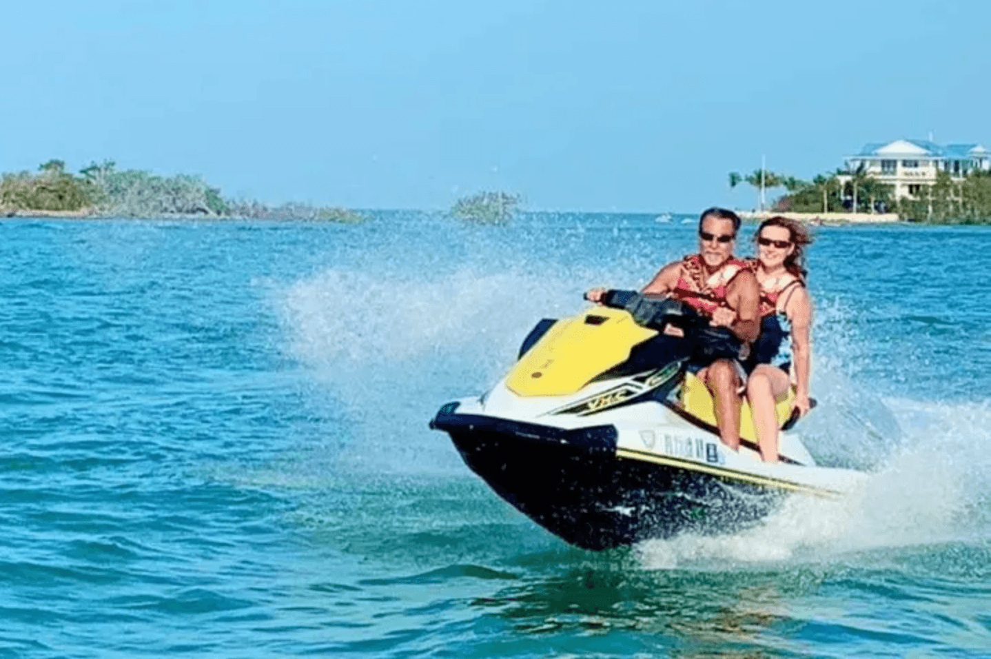 Two riders speeding on yellow jet ski across blue ocean spray