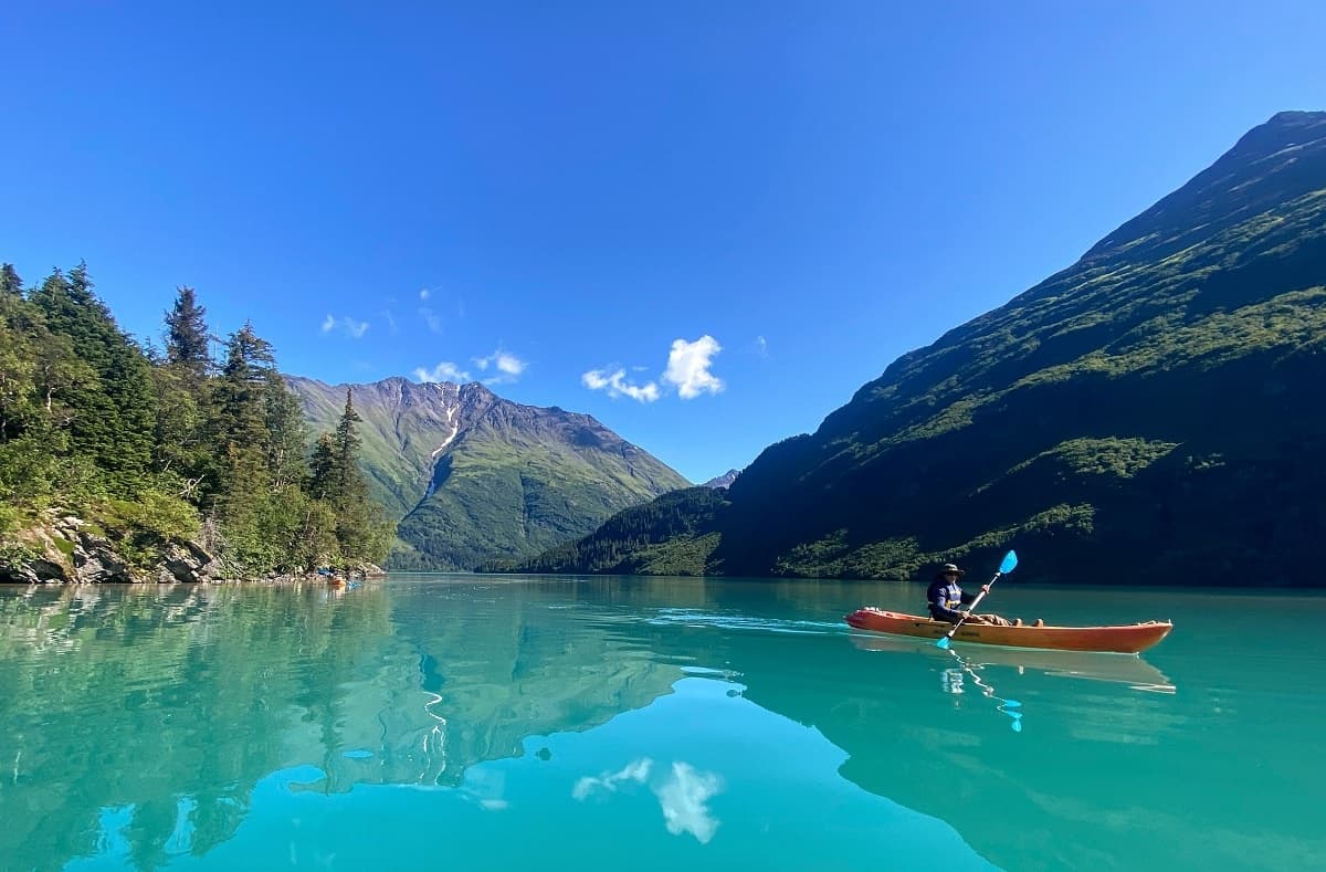 Solo kayak drifting on clear turquoise mountain lake