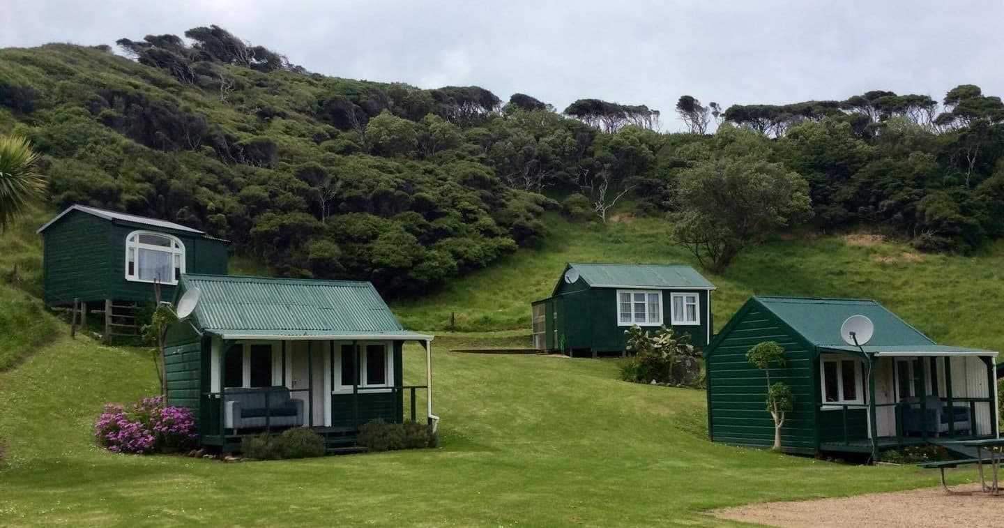 Small green holiday cabins overlooking grassy bay at Ruapuke Motor Camp