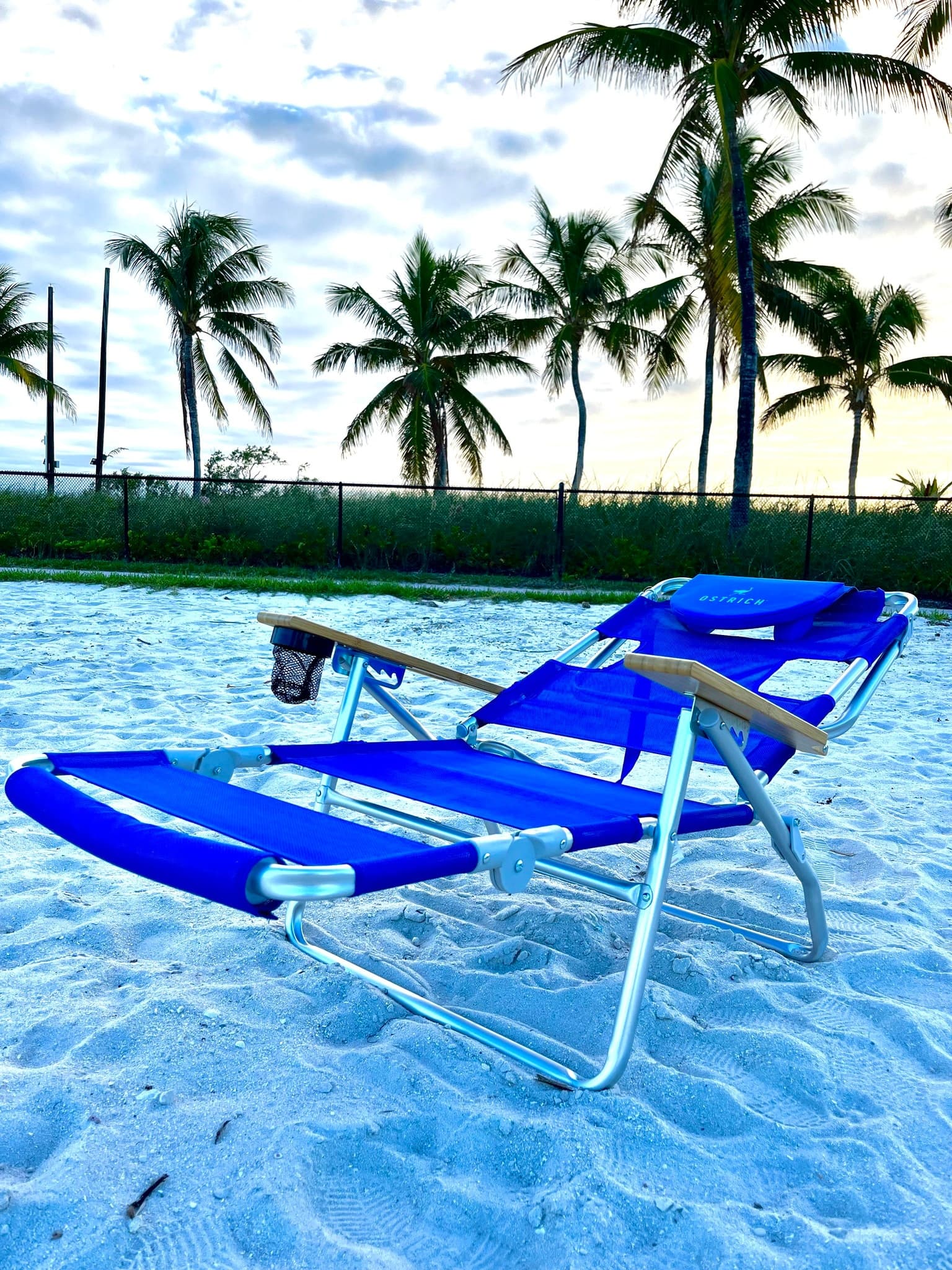 Blue reclining beach chair on white sand with palm trees