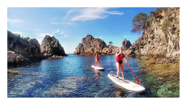 Stand-up paddleboarder surfing small waves near rocky headland