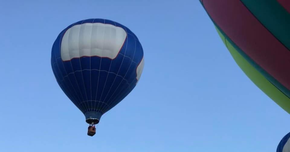Blue hot air balloon floating in clear daytime sky over plains