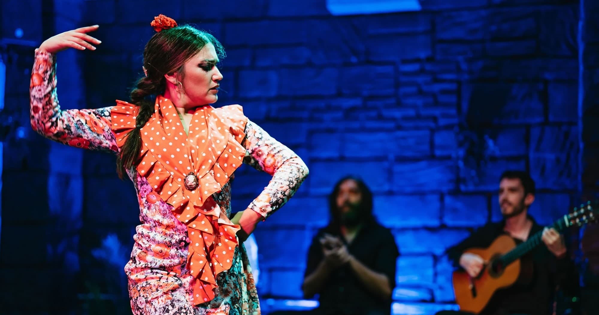Flamenco dancer performing on indoor stage with live guitarists