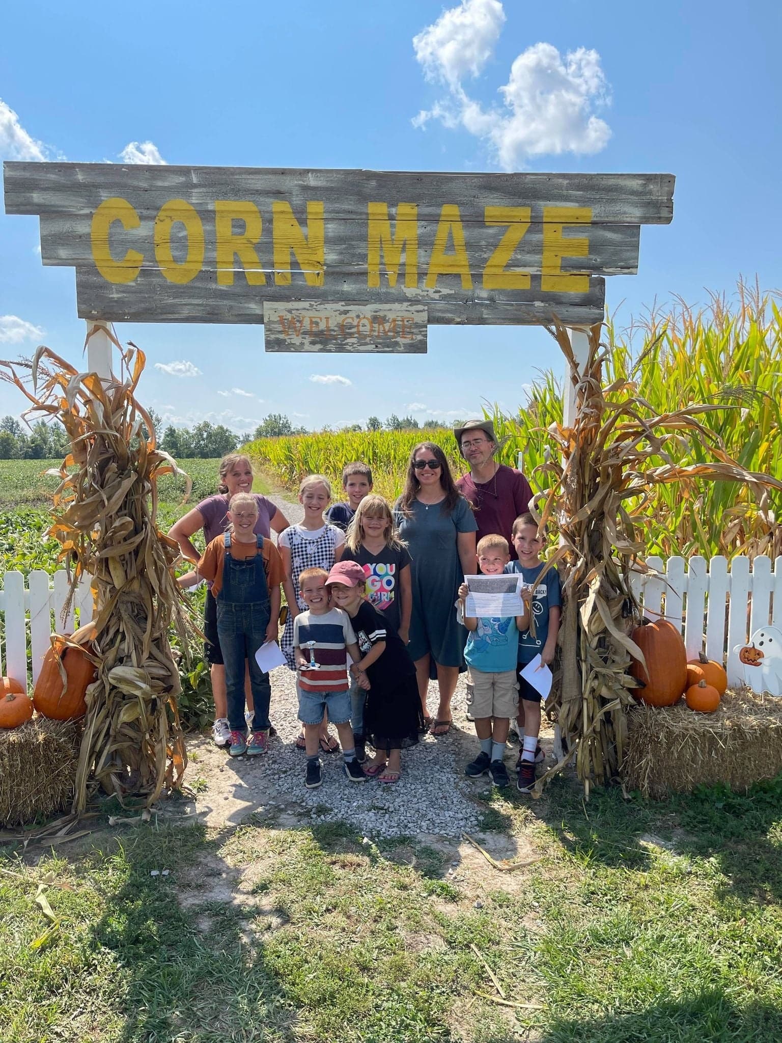Family posing at corn maze entrance with pumpkins and blue sky