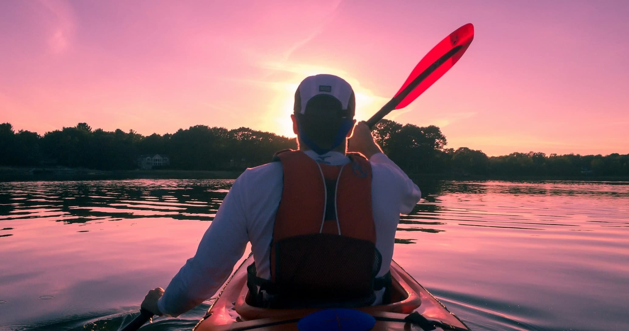 Solo kayaker paddling toward sunset on still lake