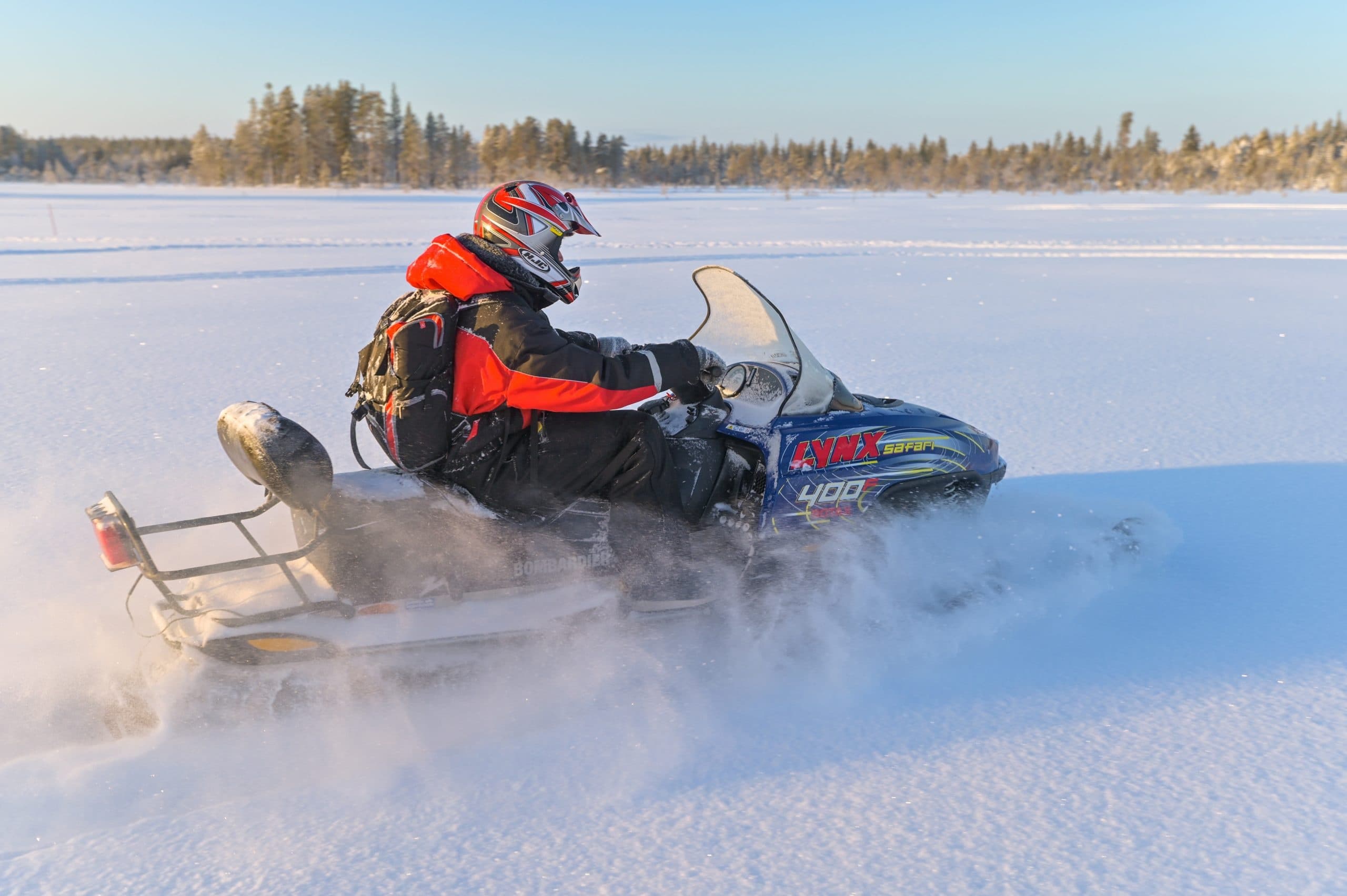 Snowmobile rider speeding across snowy frozen lake in winter forest