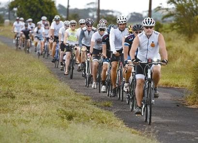 Long single-file bike group pedaling down scenic Maui country road