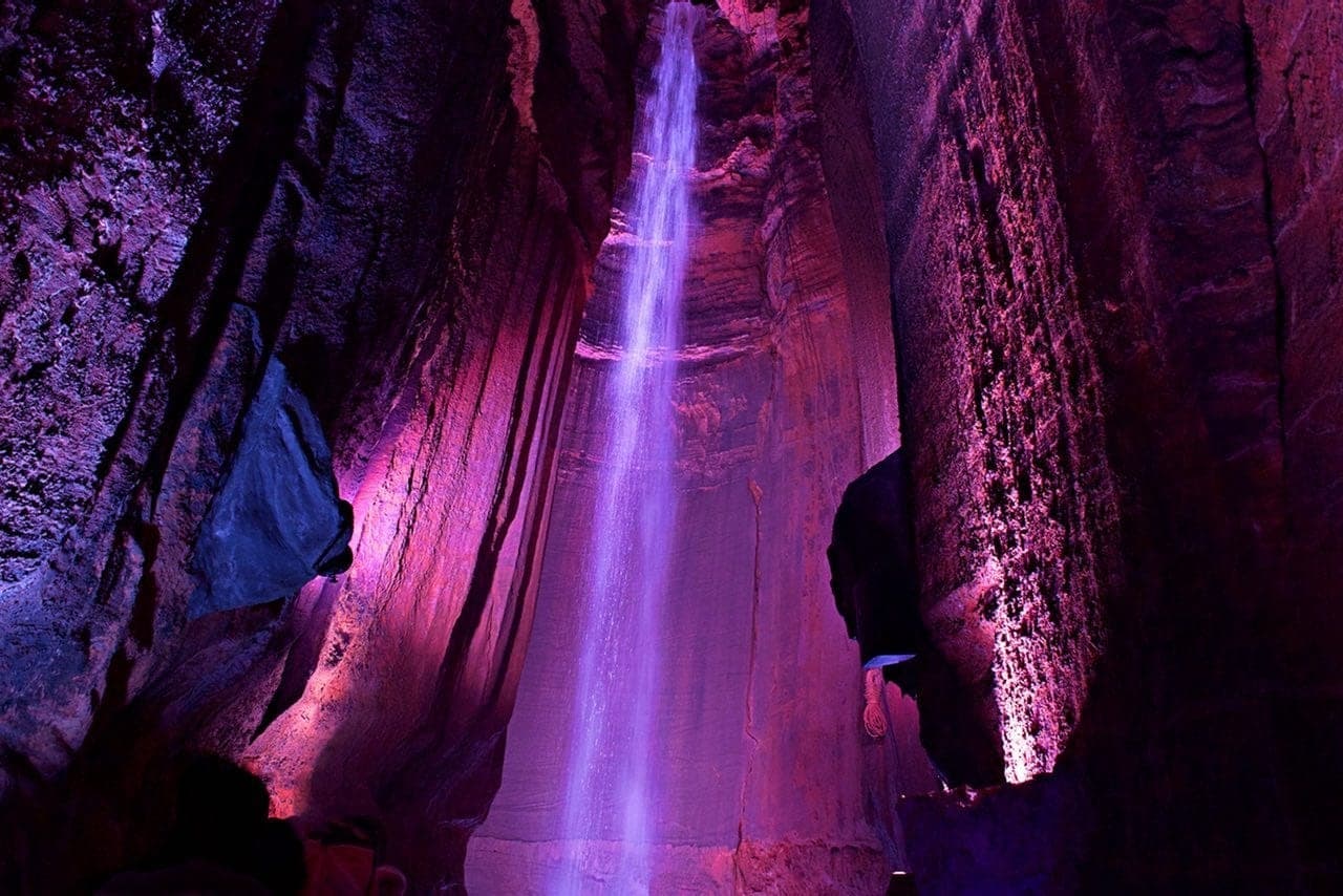 Illuminated underground cave waterfall with colorful light display