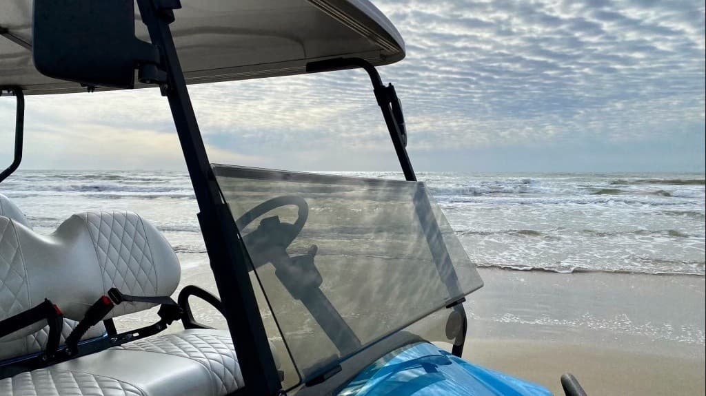 Golf cart with windshield parked on sandy beach shore