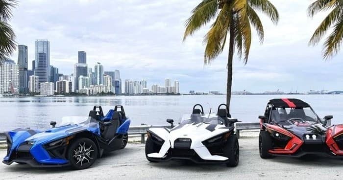 Three slingshot vehicles parked by Miami skyline waterfront