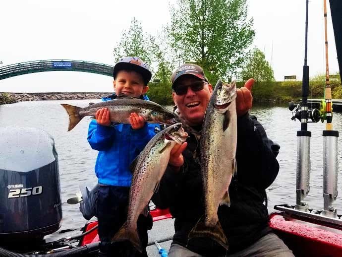Father and son holding large trout on fishing boat by river