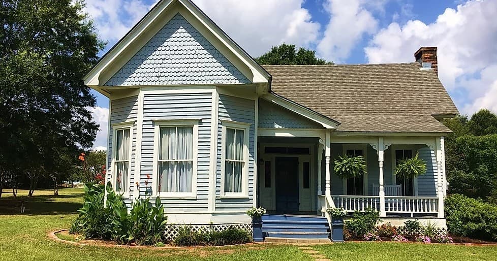 Victorian farmhouse with wraparound porch and lawn, rural