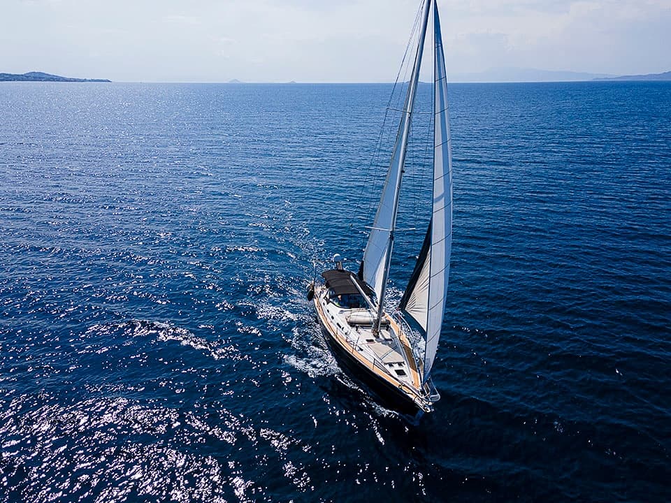 Sailboat sailing on open deep-blue sea, aerial action shot