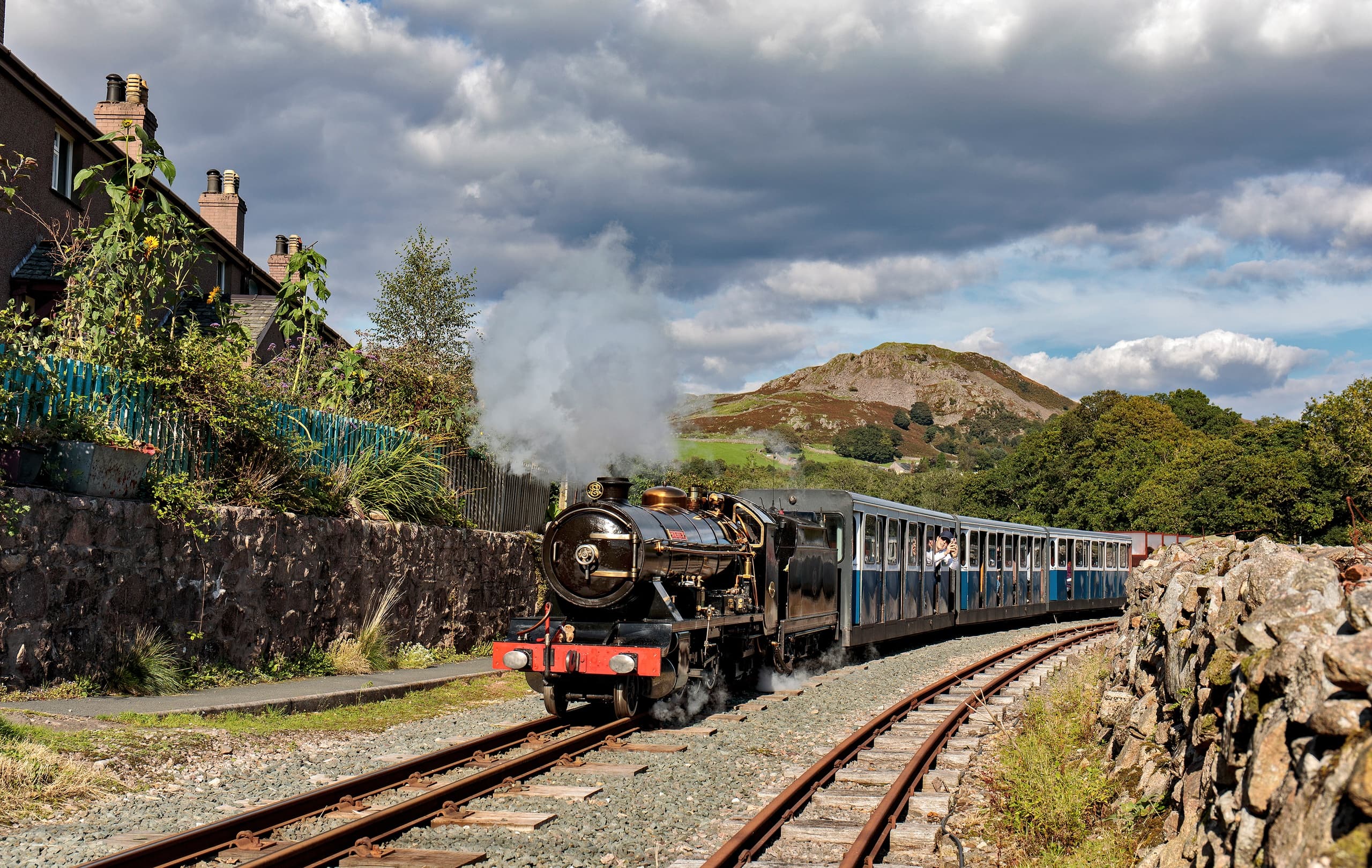 Vintage steam train rounding track under cloudy Lake District skies