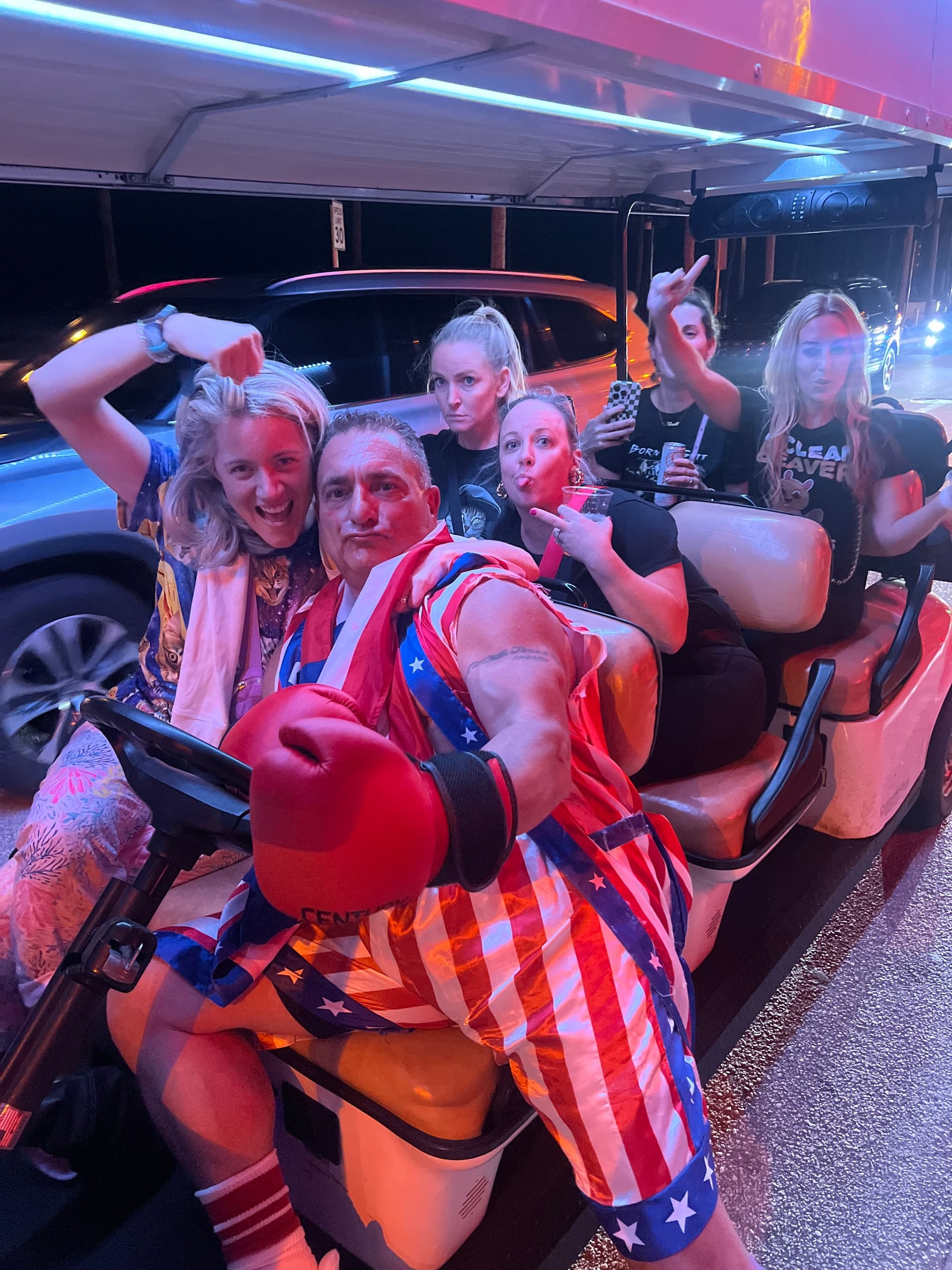Group riding a party golf cart at night on urban street