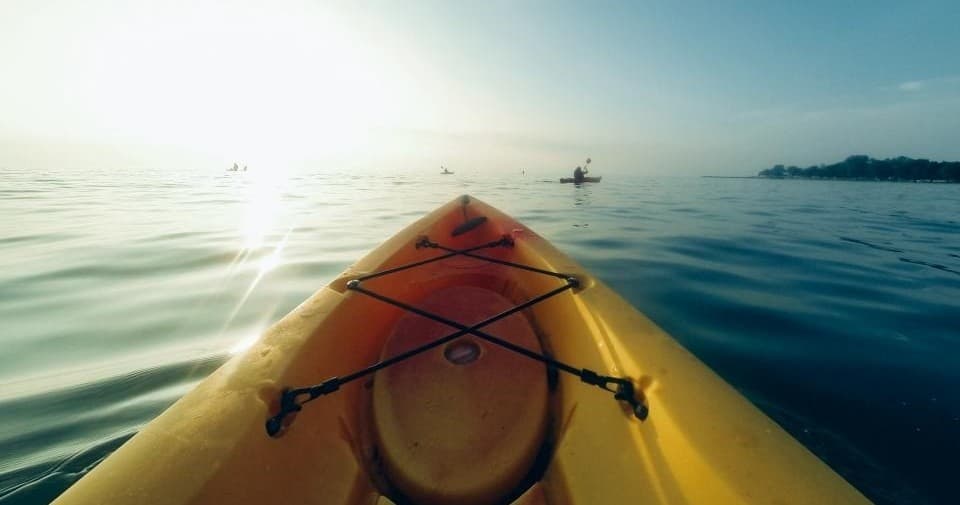 Kayak bow view on calm lake with sunrise glare