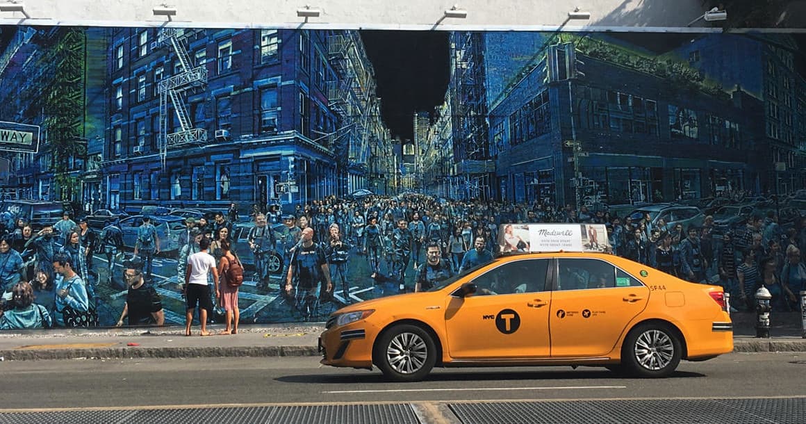 Yellow taxi passing mural on urban street in NYC neighborhood