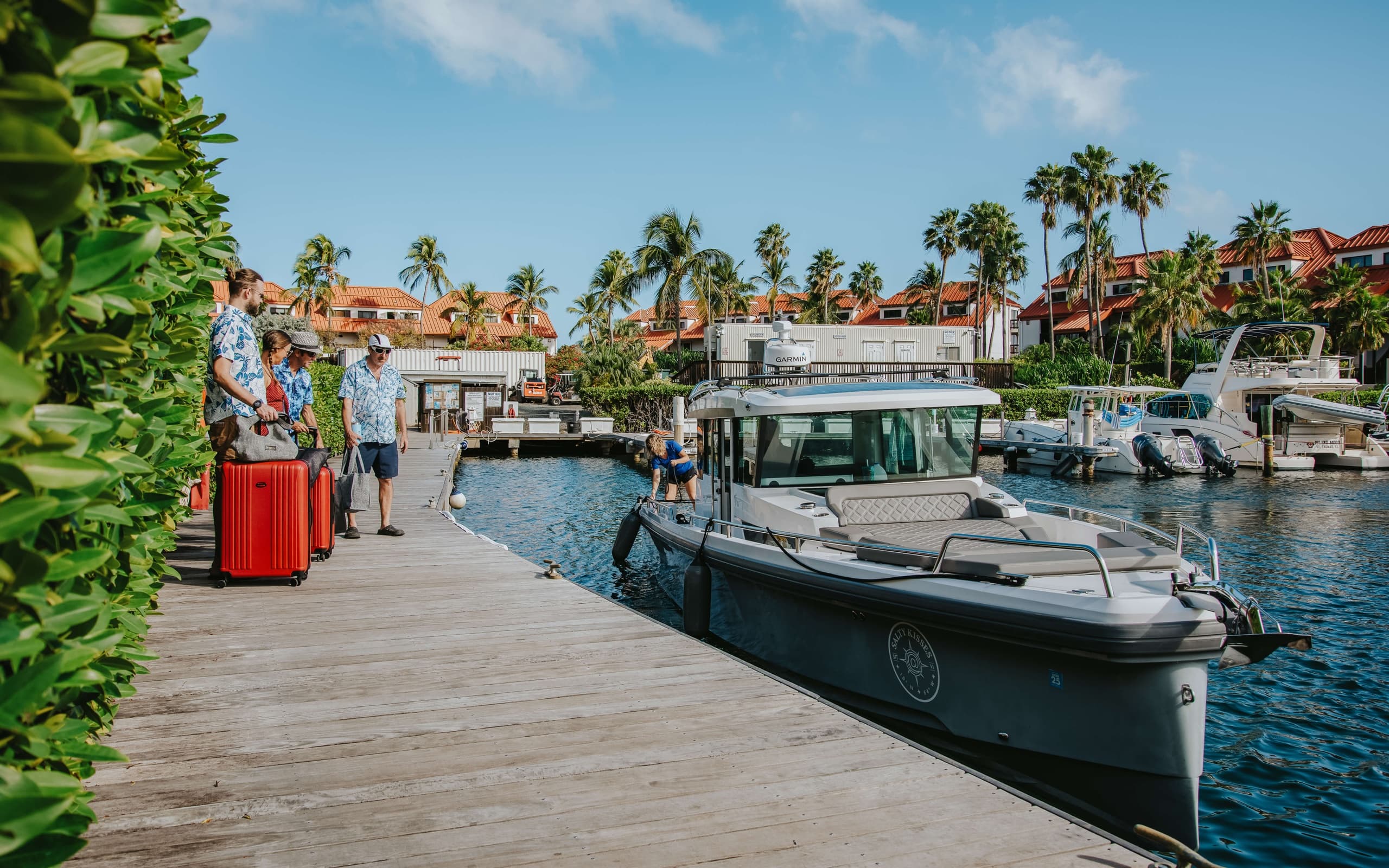 Passengers boarding motorboat at tropical marina dock with luggage