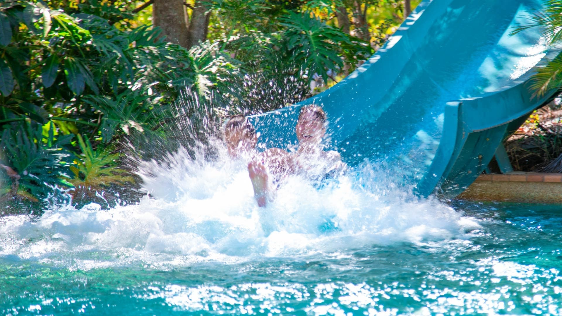 Person splashing into pool from water slide at outdoor park