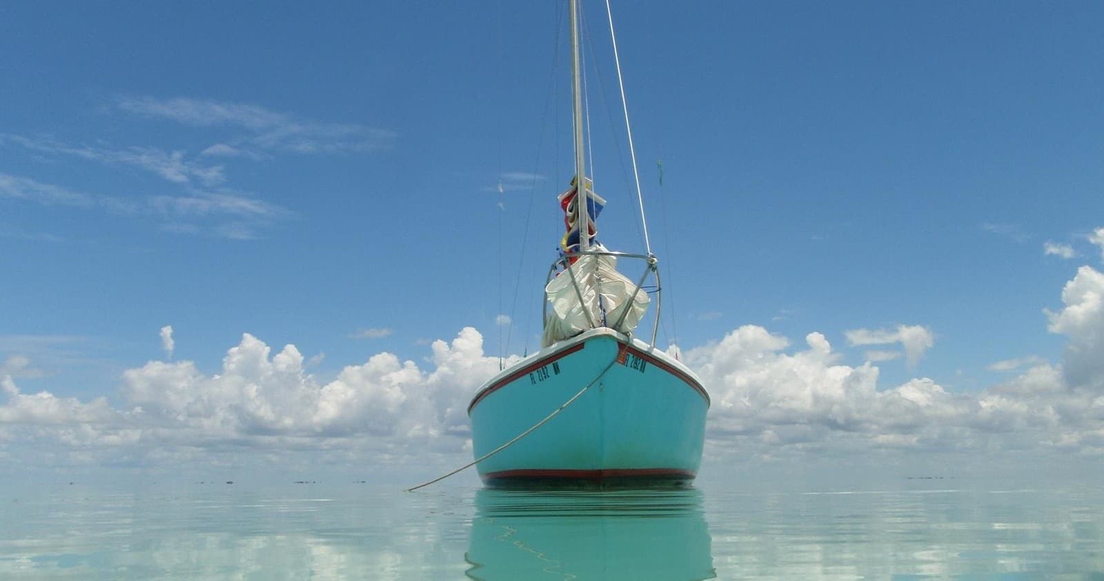 Small sailboat anchored in shallow turquoise Caribbean waters