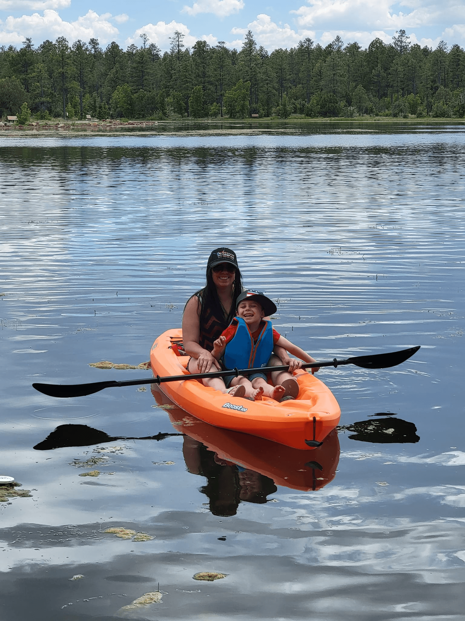 Parent and child kayaking on calm lake surrounded by pines