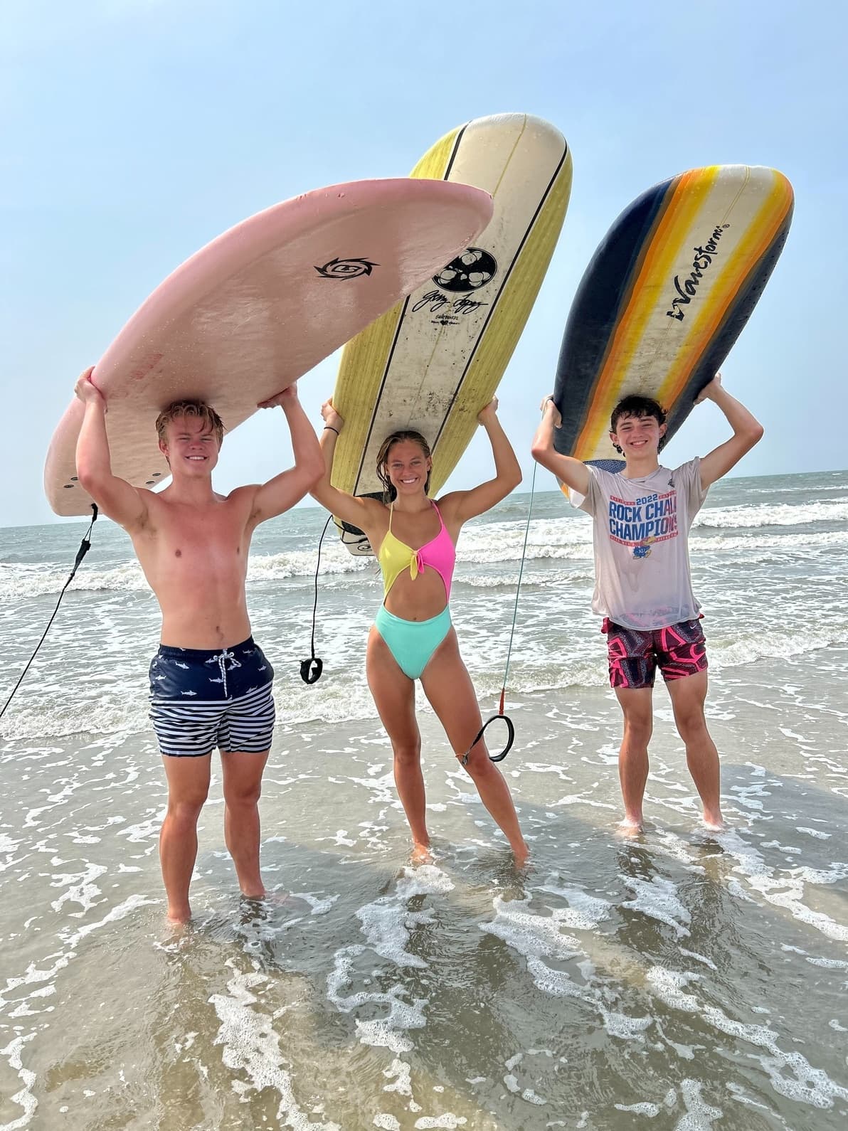 Three surfers lifting boards above heads in waist-deep ocean