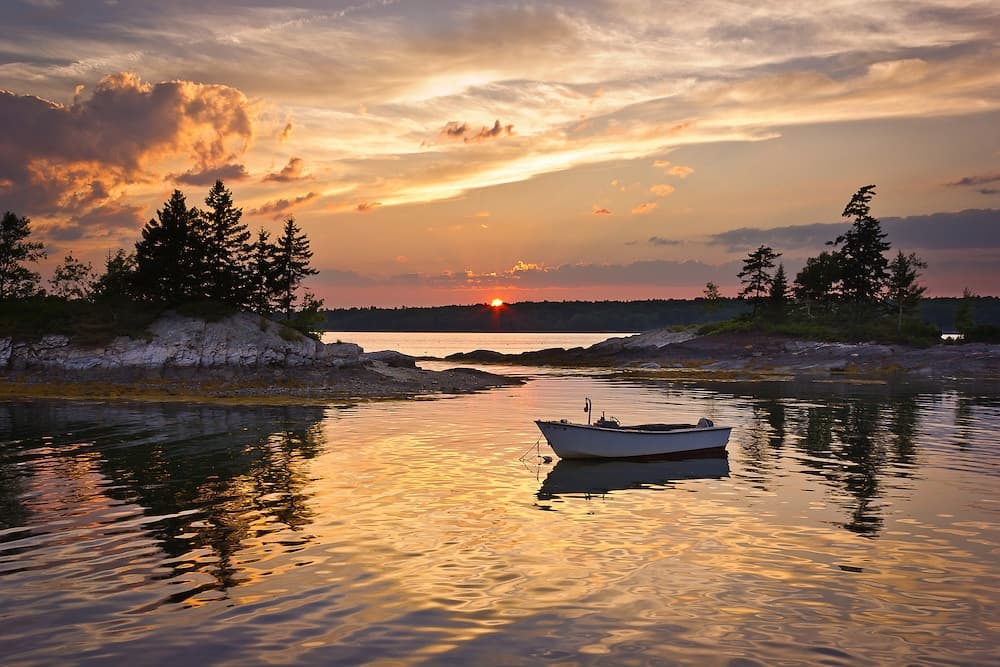 Sunset over tranquil bay with small rowboat and islands
