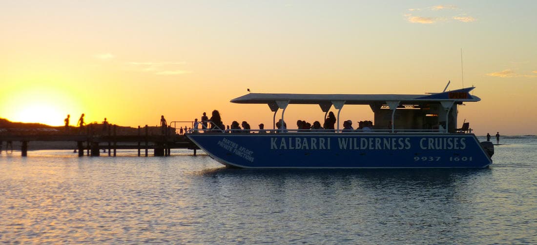 Tour boat silhouetted at golden sunset over calm coastal waters