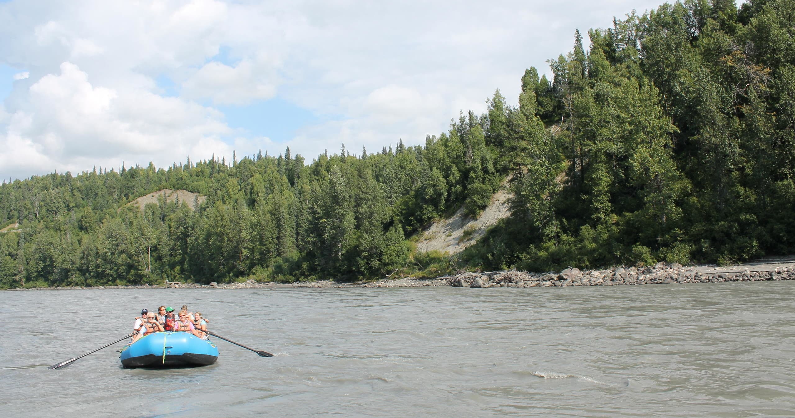 Small rafting group paddling on river near forested Alaskan banks