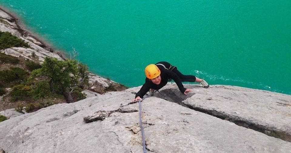 Rock climber ascending cliff above turquoise alpine lake