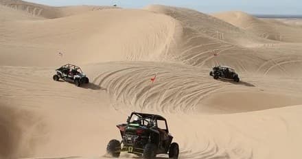 Group of UTVs crossing rolling sand dunes, guided off-road ride