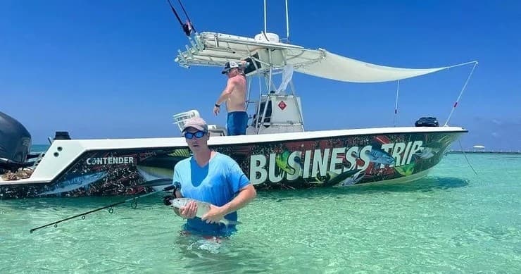 Angler wading by branded charter boat on shallow sandbar