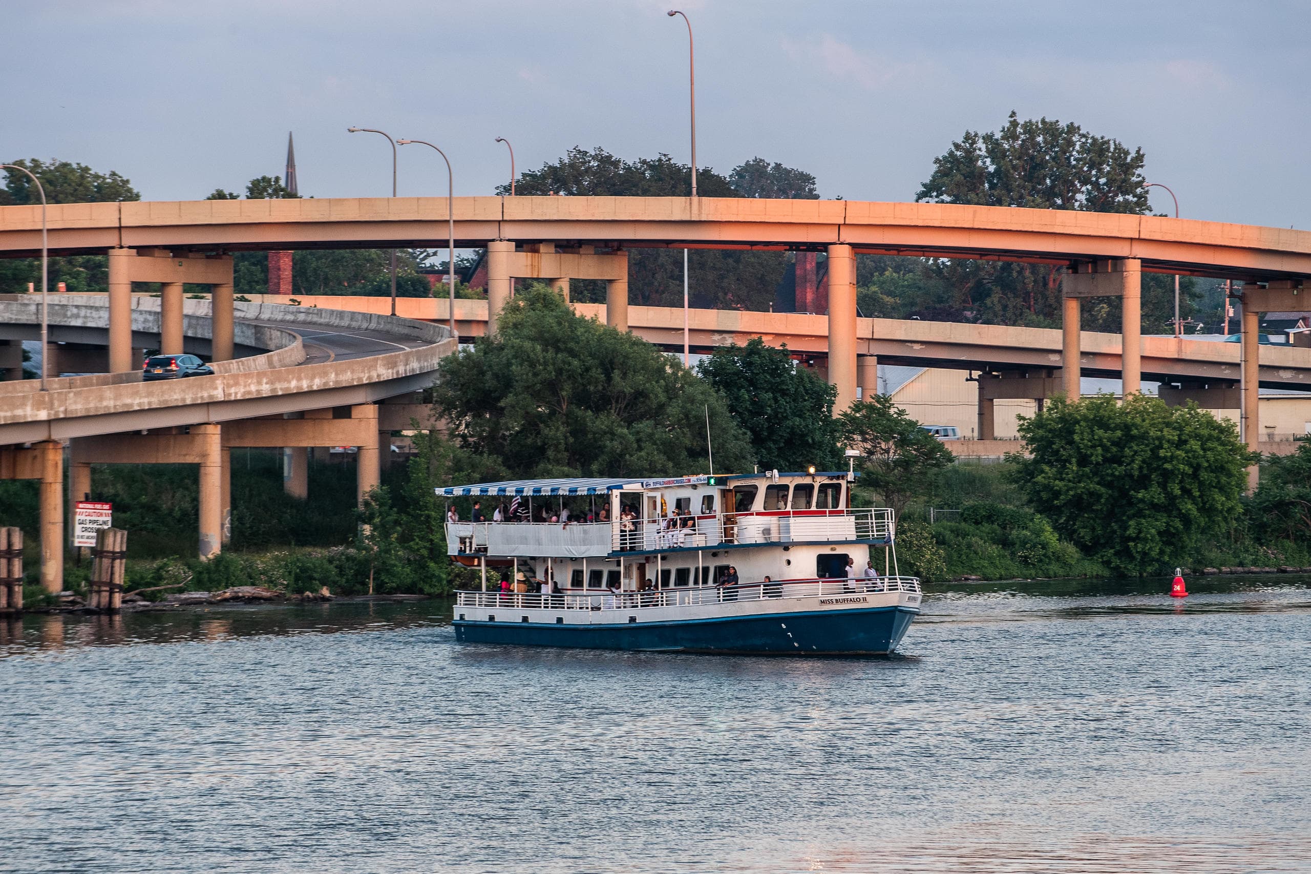 River cruise boat navigating beneath elevated highway in city