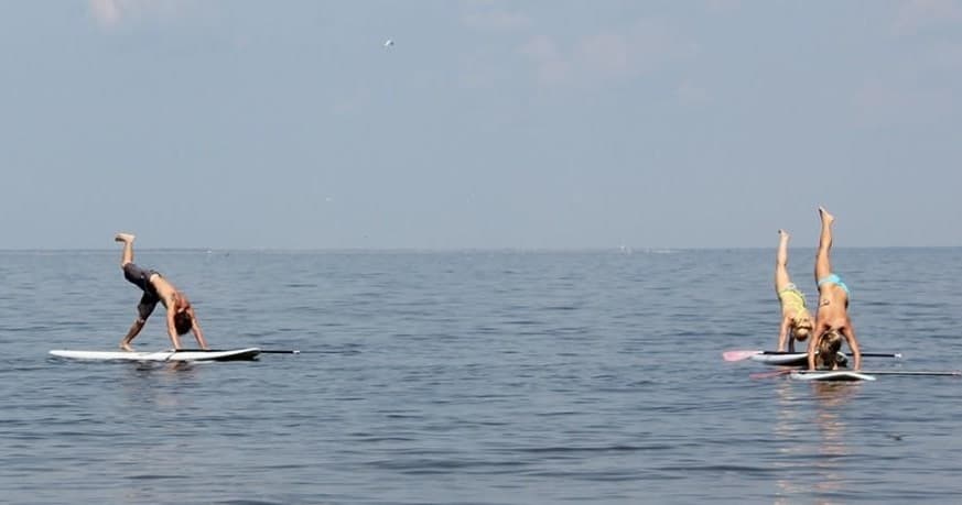 Standup paddleboarders doing handstands on calm ocean water