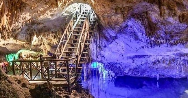 Visitors exploring illuminated cenote cave pool with wooden stairs in Akumal