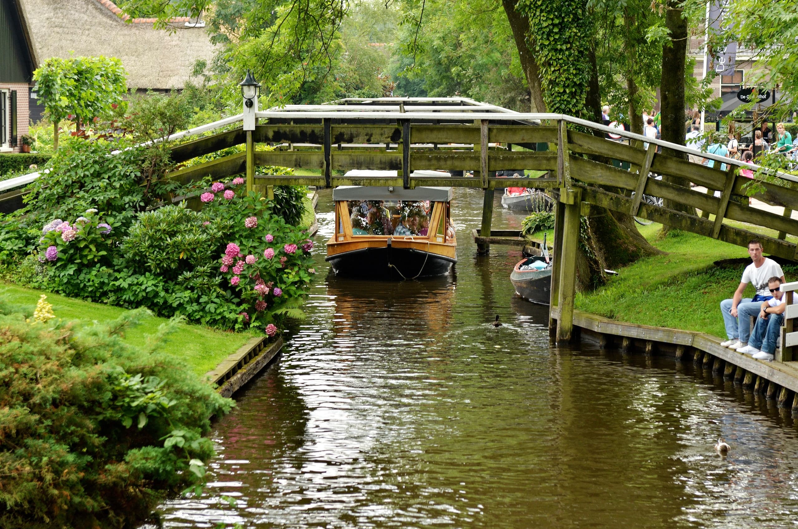 Tour boat passing under wooden bridge in Giethoorn canals