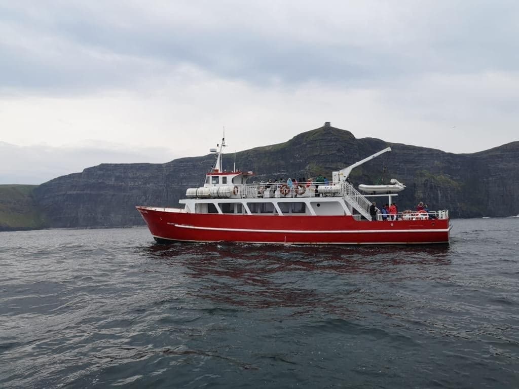Red sightseeing boat cruising near rugged sea cliffs off Galway