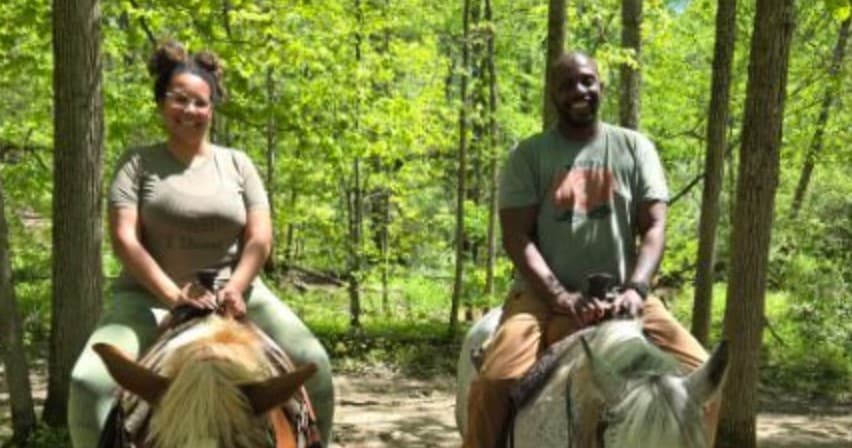 Two people trail riding on horses through green forest trails
