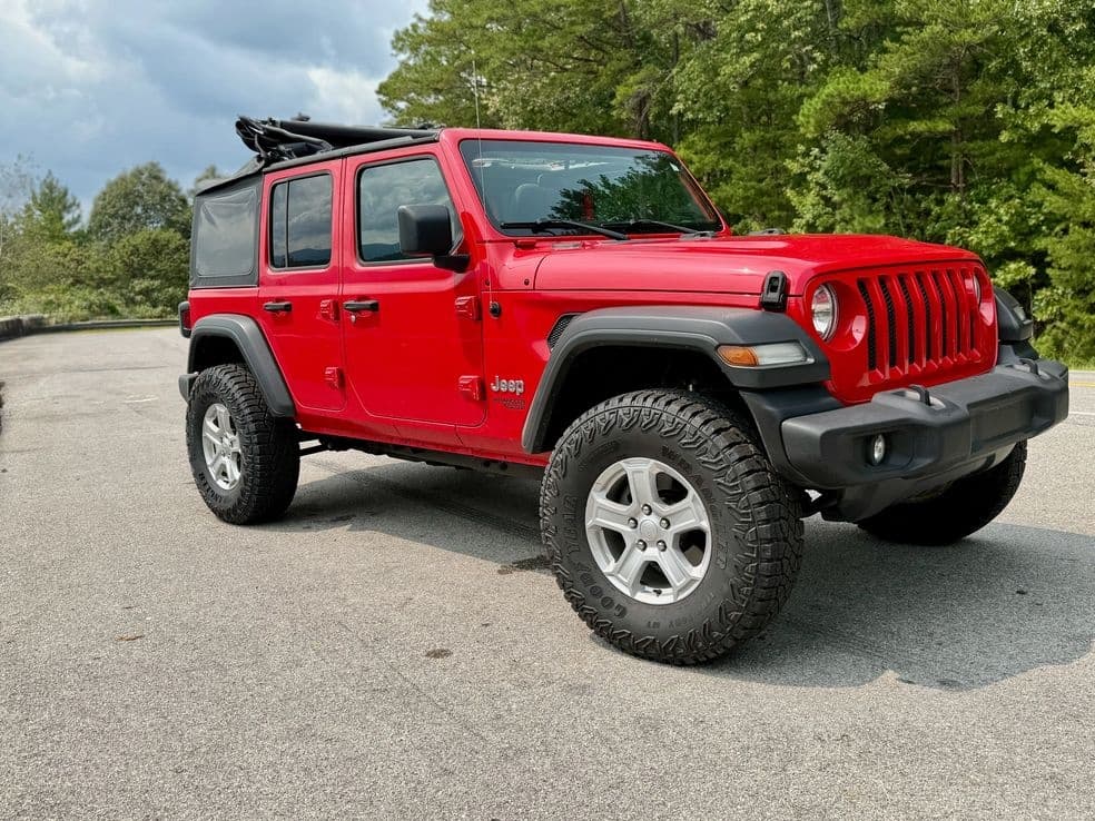 Red Jeep Wrangler angled in forested lot, off-road adventure ready
