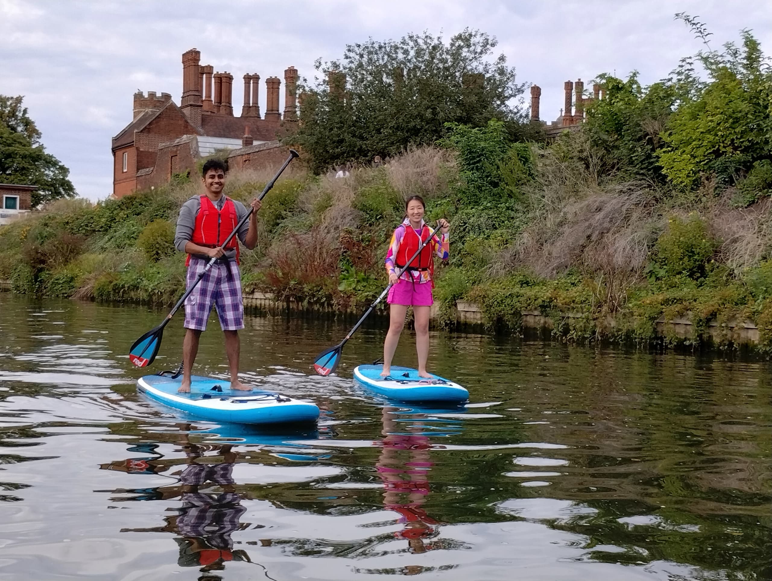 Two stand-up paddleboarders paddling near riverside houses