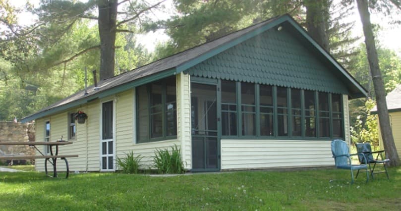 Screened porch cabin on grassy waterfront lot with chairs