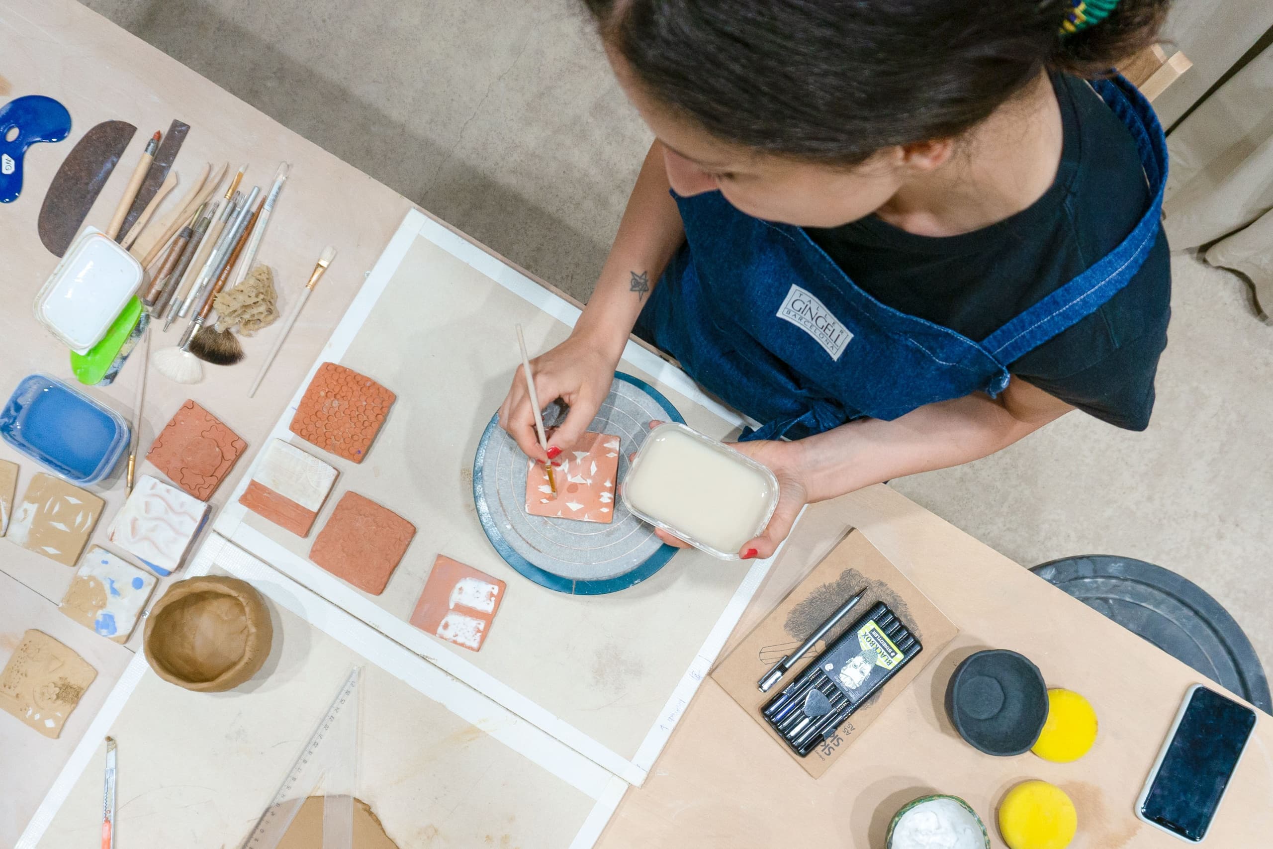 Overhead view of ceramic tiles and glazes on studio workbench